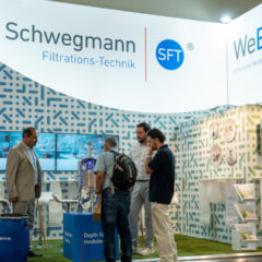 Vier Männer stehen an einem Messestand von Schwegmann Filtrations-Technik und WeBaX und unterhalten sich.