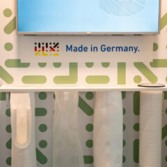Ausstellungsständer mit Filterbeuteln, einem aufgerollten Filter und einem Fernsehbildschirm über dem Schriftzug „Made in Germany“.